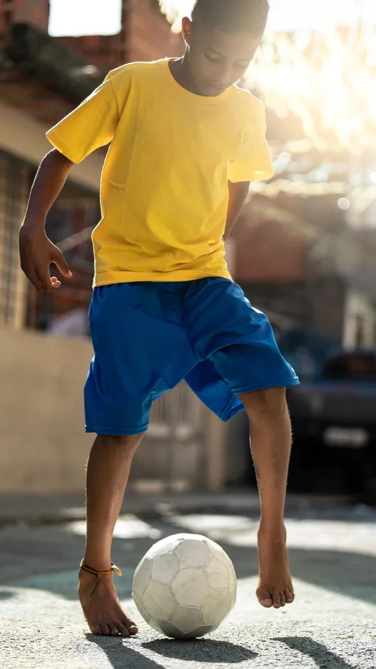 Ragazzo con maglia gialla e pantaloncini blu che gioca a calcio